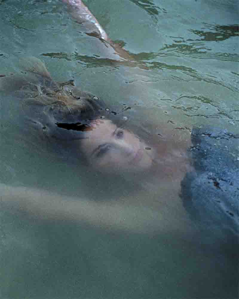A woman peacefully floating in calm water, embodying tranquility and relaxation in a natural setting.