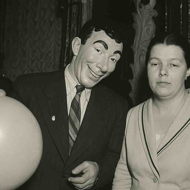 A man and woman stand side by side, both smiling and holding a bright balloon, capturing a joyful moment together.